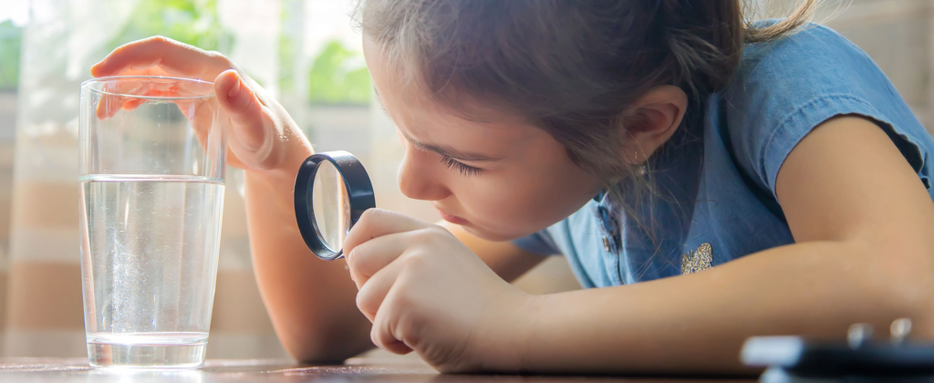 Une fillette qui regarde un verre d'eau à travers une loupe.